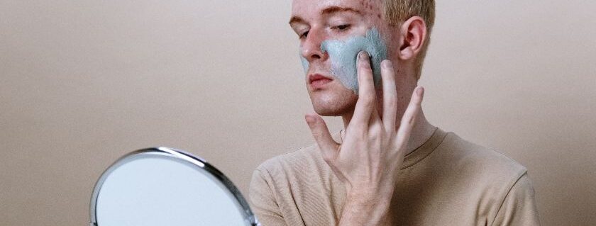 man applying facial mask cream in front of mirror