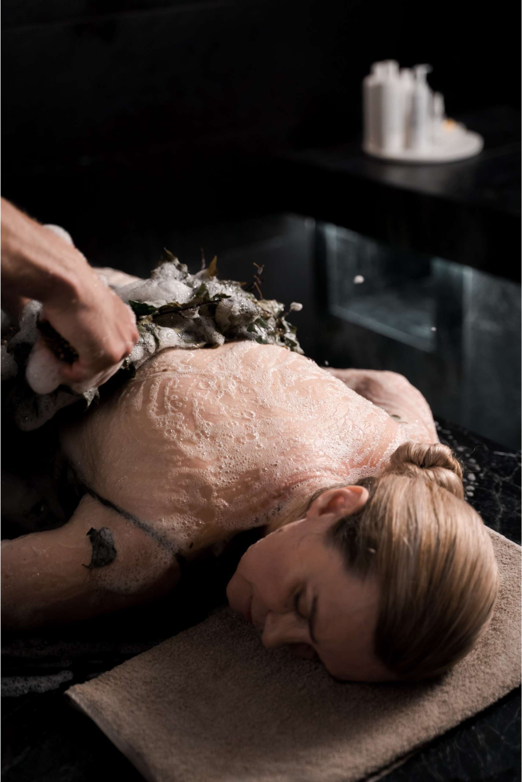 woman having back massage with leaves and bubbles