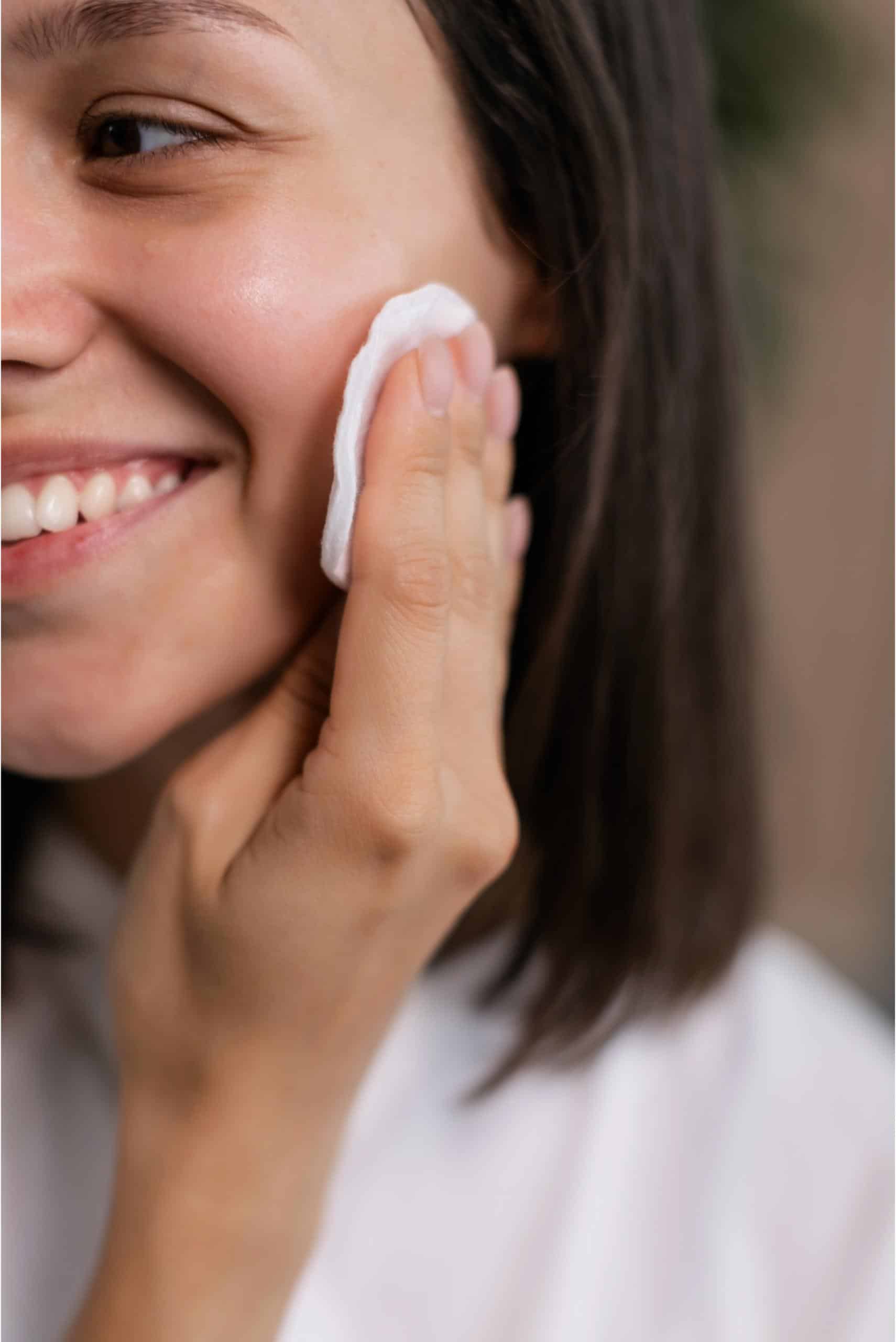 woman smiling while wiping her face with cotton