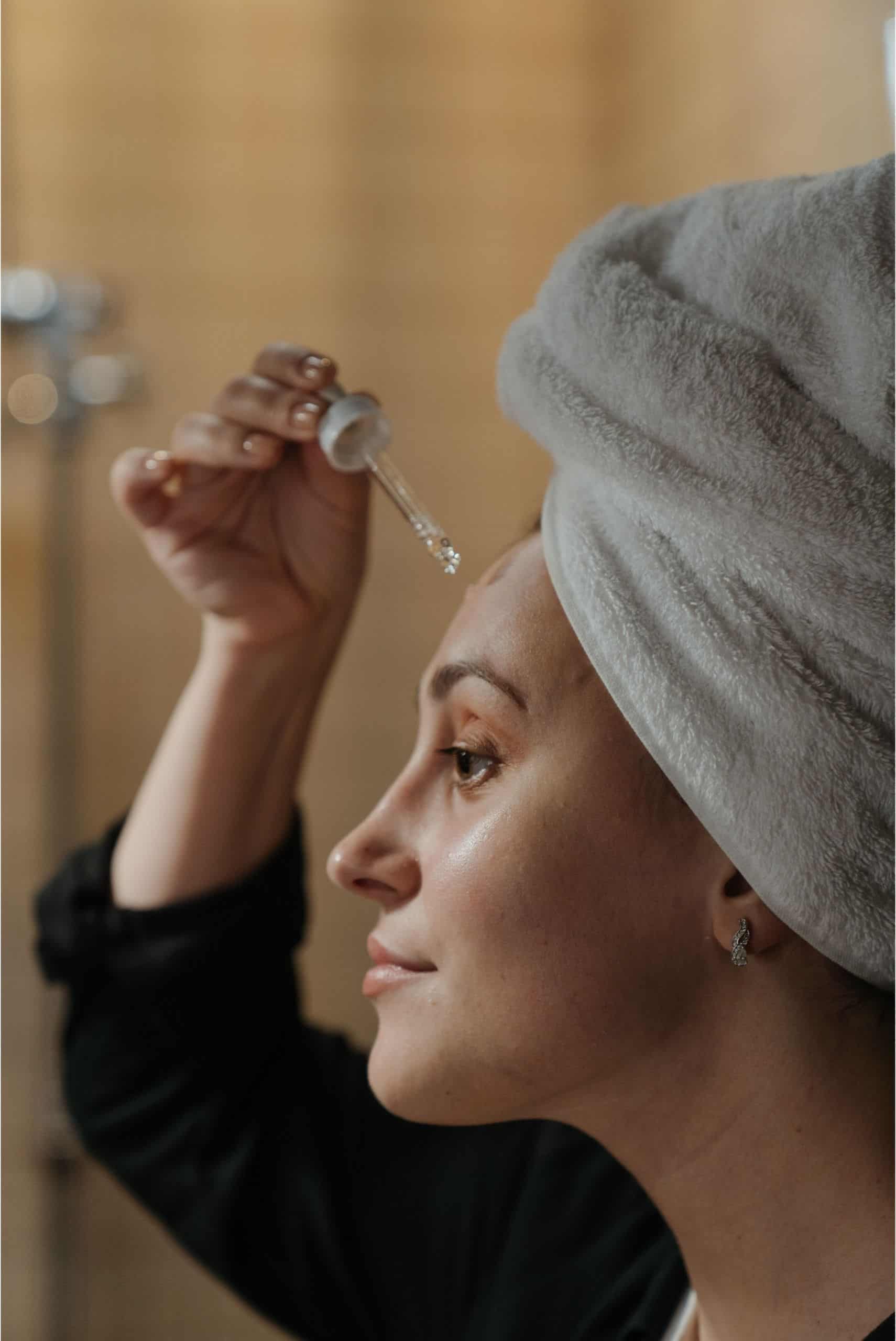 woman with towel head applying serum on face